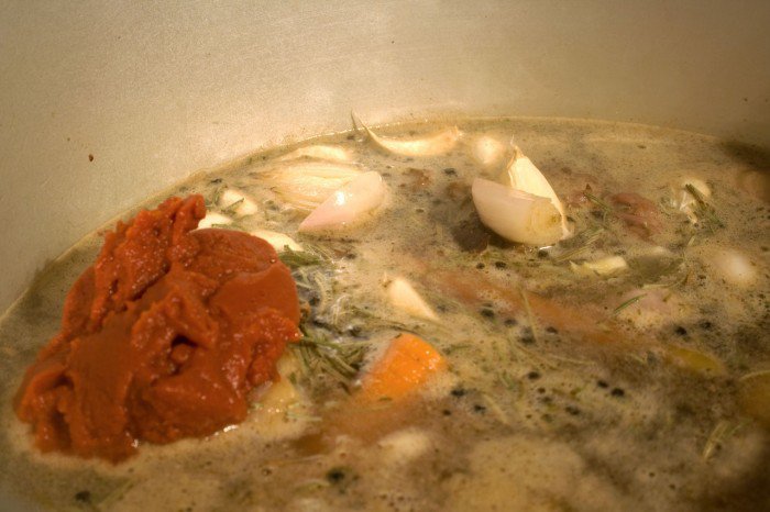Tomatpuree, skalotteløg, et fed hvidløg, rosmarin og peberkorn lagt i vandet til de brunede oksehale stykker
