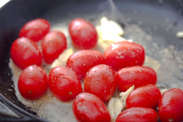 Tomaterne ligges hele ned når smøret er smeltet. Hvidløg tilsættes og de drysses med salt