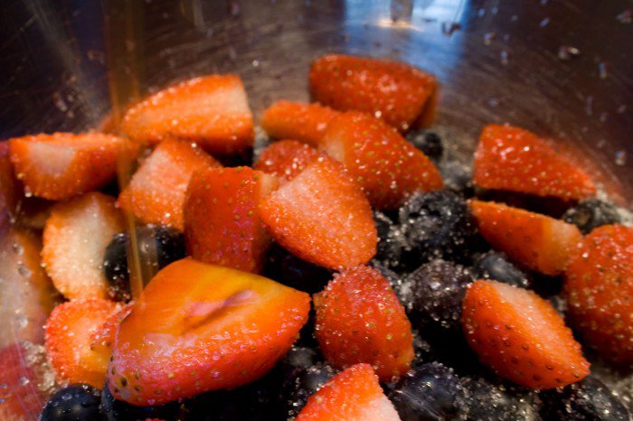 Halverede jordbær og blåbær med sukker og vaniljeekstrakt